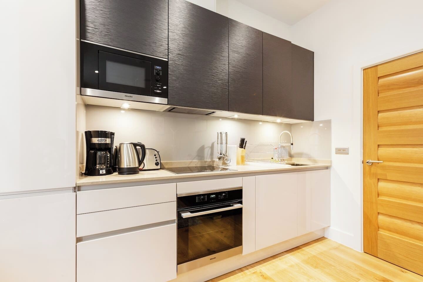 A compact kitchen with a microwave, coffee maker, toaster, sink, and oven.