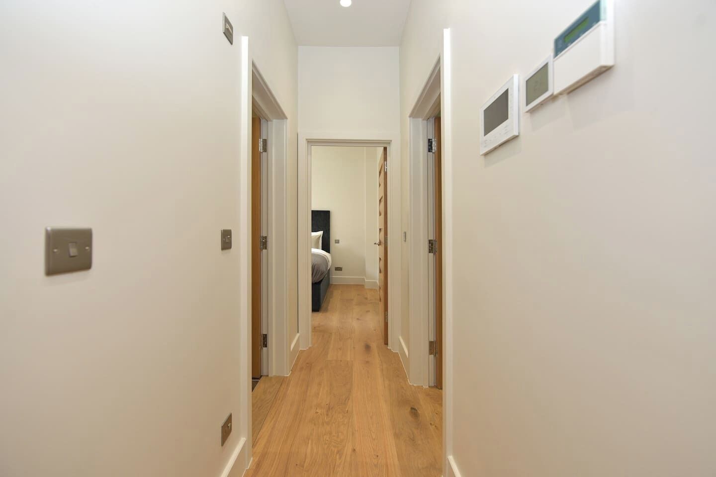 A narrow hallway with wooden flooring, white walls, and doors leading to bedrooms.