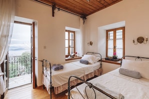 A bedroom with two beds, a balcony, and a view of the outdoors. - Stone Villa in Koukourava Pelion with Private Pool and Panoramic Sea Views (koukourava)