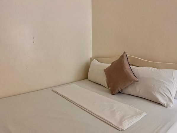 A bed with white bedding and a single brown pillow.