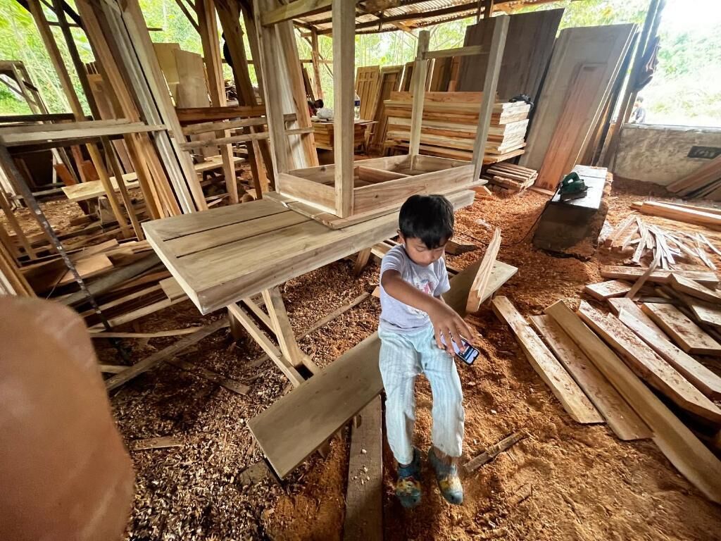 Un niño sentado sobre una estructura de madera rodeado de diversas tablas y vigas.