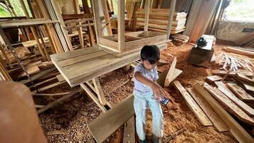 Un niño sentado sobre una estructura de madera rodeado de diversas tablas y vigas.