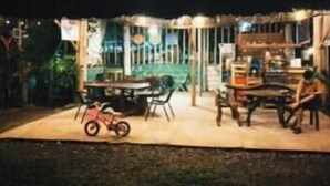 Un espacio al aire libre con mesas y sillas, una bicicleta y una mesita con un juguete infantil.