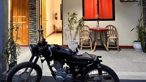 Una motocicleta estacionada en una habitación con una puerta de madera, una cortina roja y una pequeña mesa con sillas.