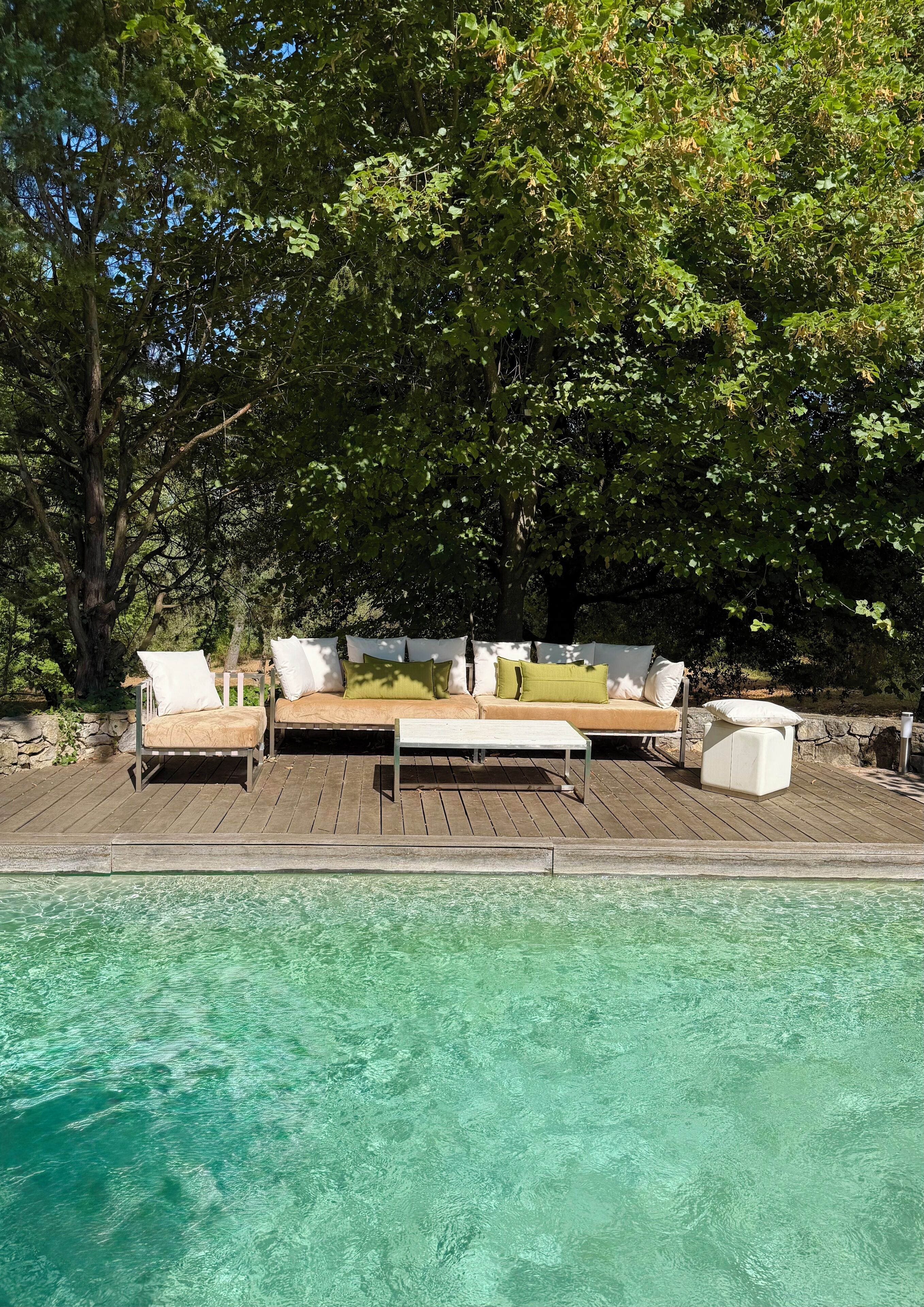 Une terrasse en bois avec un canapé et des fauteuils, donnant sur une piscine aux eaux cristallines.