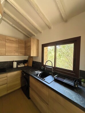 Eine Küche mit Holzausstattung, einer schwarzen Arbeitsplatte, einem Fenster mit Blick auf Grünflächen und einem Spülbecken mit Armatur.