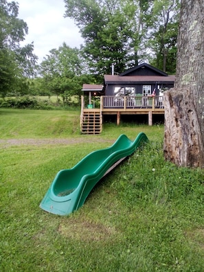 A wooden deck with a green slide, a cabin, and a tree. - Weber Hill Farm Cabin in Bovina! Operating Dairy Farm visits available with stay (Bovina Center)