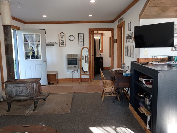 A room with a wooden floor, a vintage stove, a mirror, a television, and a bookshelf.