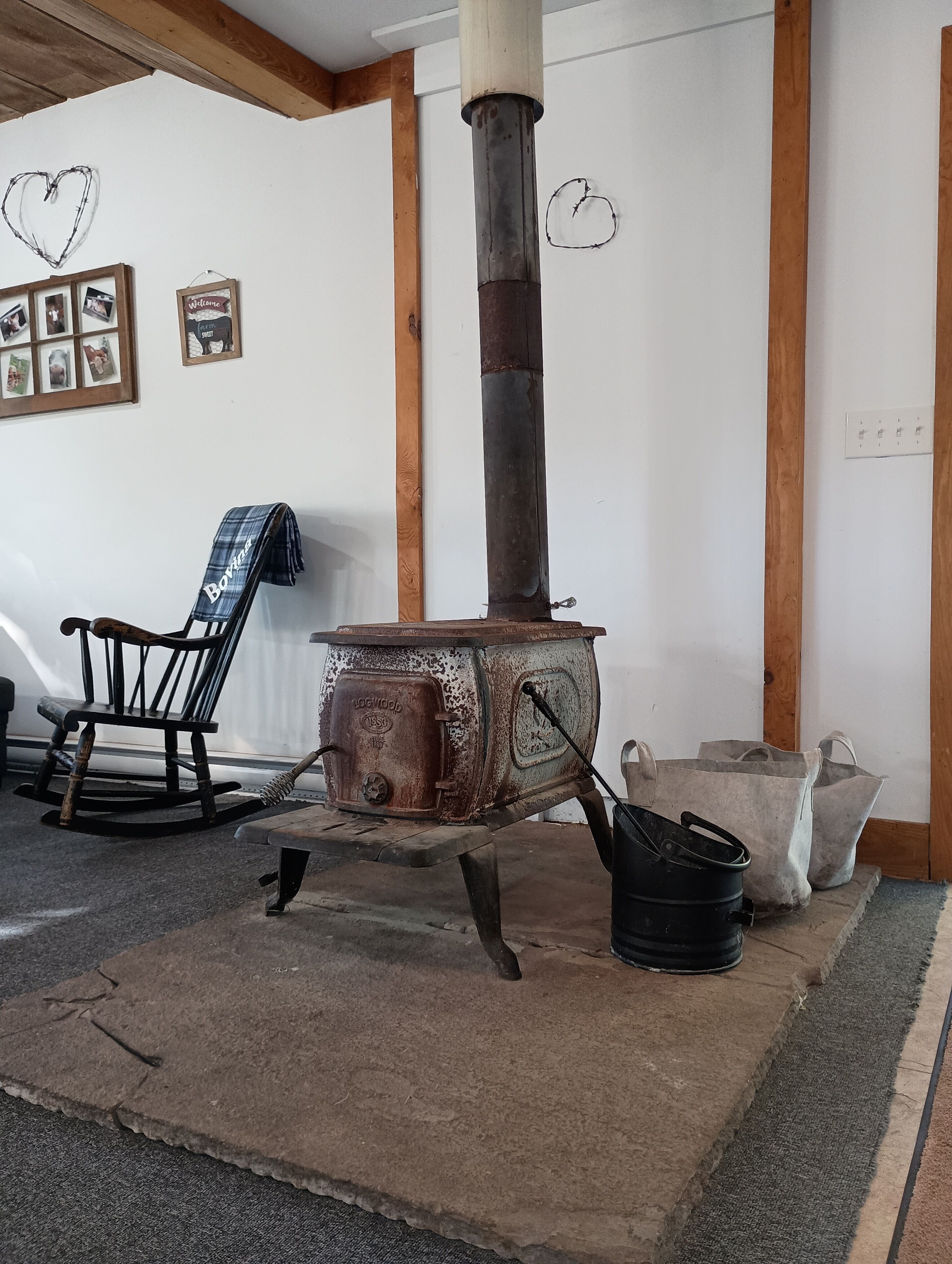 A rustic room with a wood-burning stove, a rocking chair, and a 'Welcome' sign on the wall.