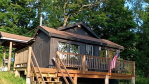 A cabin with a wooden deck, a staircase, and a flag.