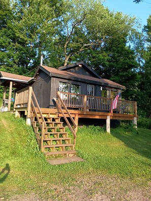 A cabin with a wooden deck, a staircase, and a flag.
