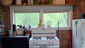 A kitchen with a stove, sink, and window overlooking greenery.