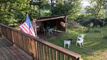 A wooden deck with a railing, an American flag, a covered outdoor seating area with tables and chairs, and a grassy yard.