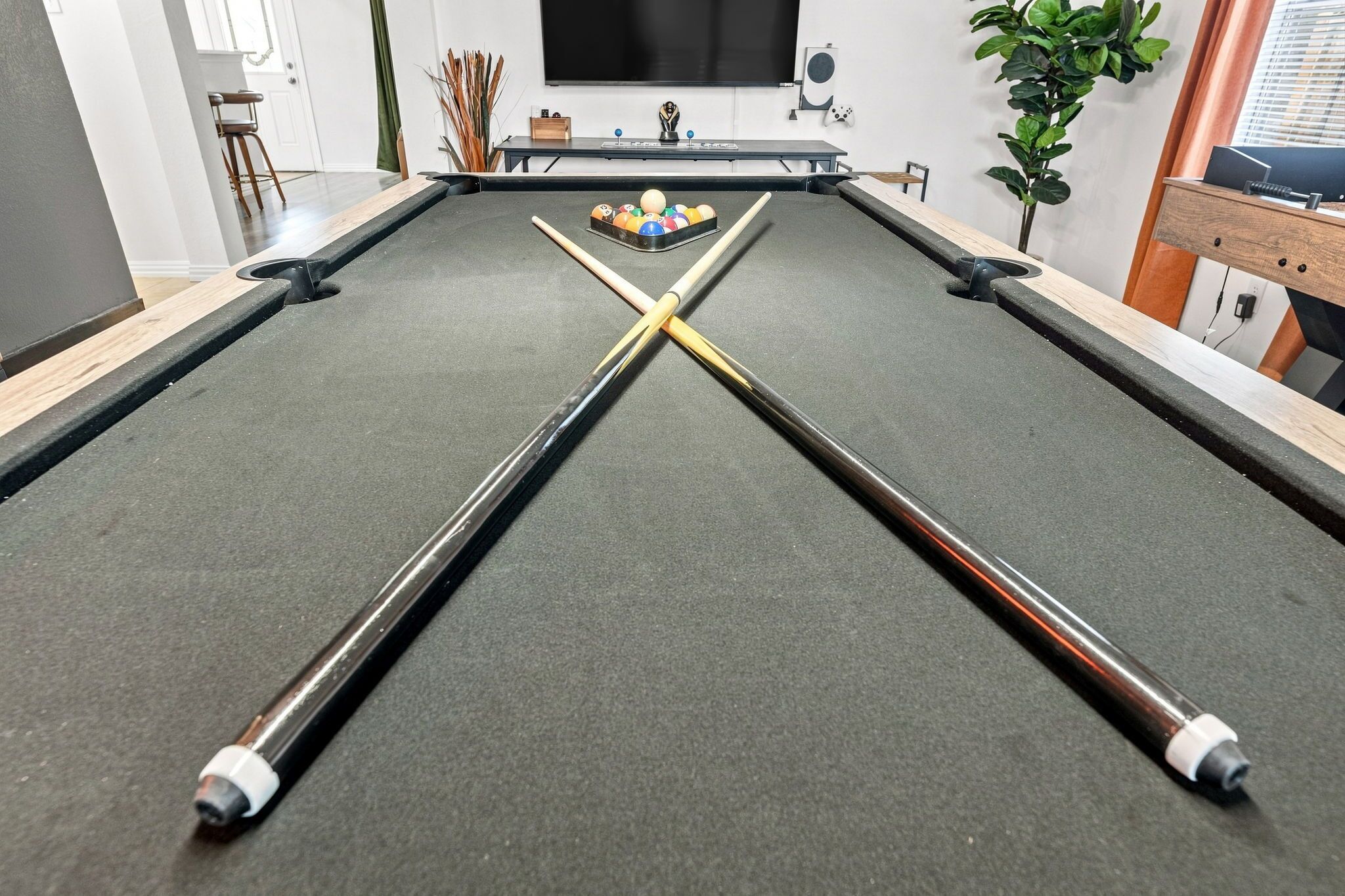 A pool table with a cue stick in the center, surrounded by chairs and a television.