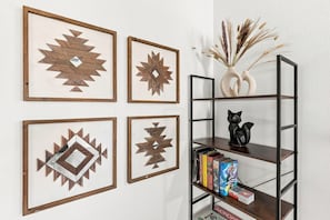 A wall with four geometric wooden art pieces and a black cat figurine on a black metal shelf with books. - Modern 4BR Home with Hot Tub and Game Room Near Fort Worth (Haltom City)