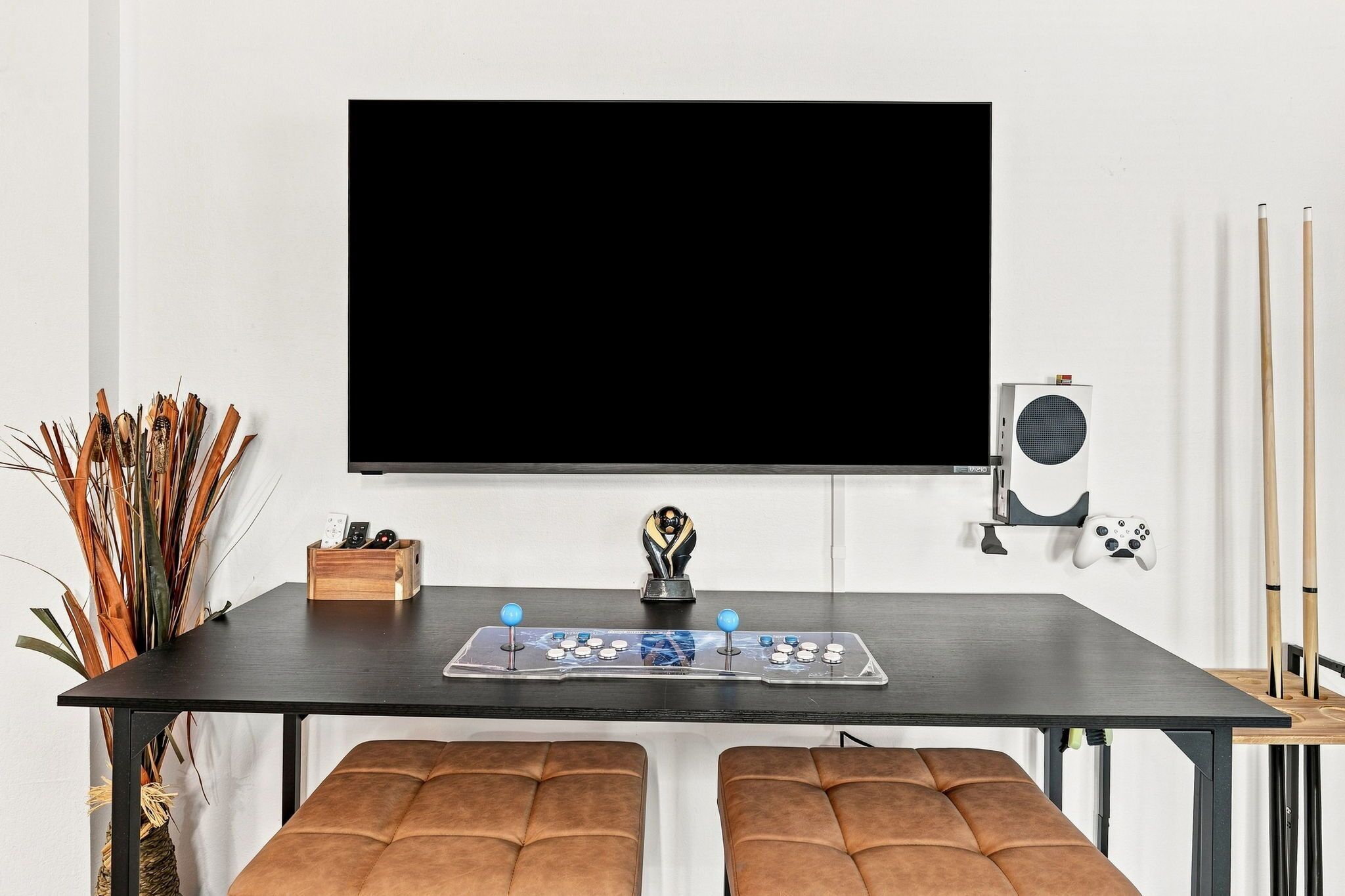 A room with a large flat-screen TV mounted on the wall, a gaming console, and a pair of drumsticks on a shelf.