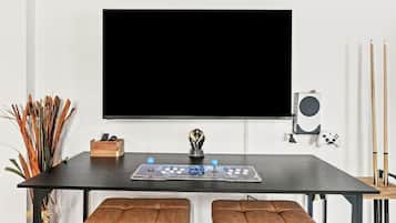 A room with a large flat-screen TV mounted on the wall, a gaming console, and a pair of drumsticks on a shelf.