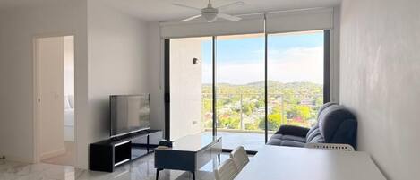 A modern living room with a flat-screen TV, a dining table, and a sofa.