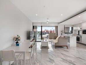 A modern kitchen with a dining area, a sofa, and a view through the glass door. - Timi Property (Woolloongabba)
