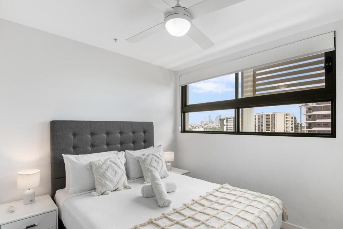 Un dormitorio con cama, mesita de noche, lámpara y ventana con persianas.