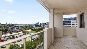 A balcony with a city view, a tiled floor, and a glass railing.