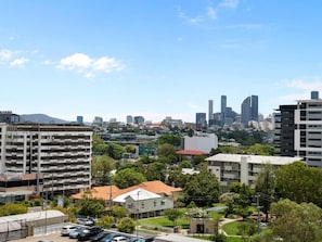 A cityscape with a mix of modern and traditional buildings, a parking lot, and green spaces. - Timi Property (Woolloongabba)