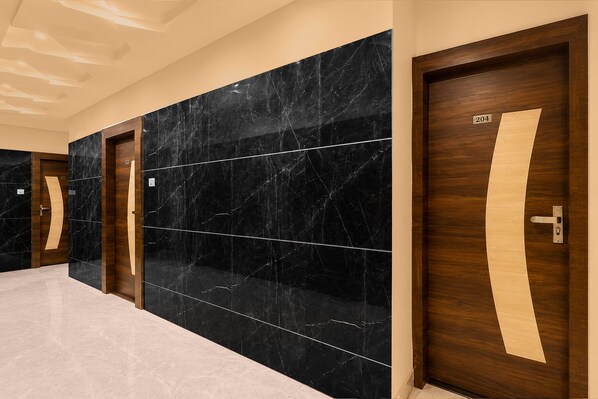 Un pasillo con paredes de mármol negro, puertas de madera y suelo de color claro.