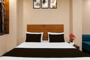 A hotel room with a wooden headboard, a bed with black and white bedding, and a nightstand with a vase of red flowers.