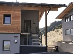 A modern building with a wooden facade, a staircase leading to a covered entrance, and a view of a hilly landscape. - Panoramic View Suite on the Kaunergrat (Kaunerberg)