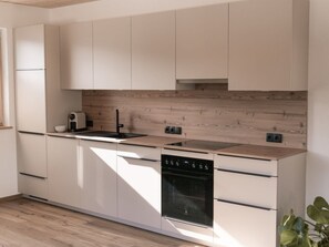A modern kitchen with white cabinetry, a wooden backsplash, and a built-in oven. - Panoramic View Suite on the Kaunergrat (Kaunerberg)
