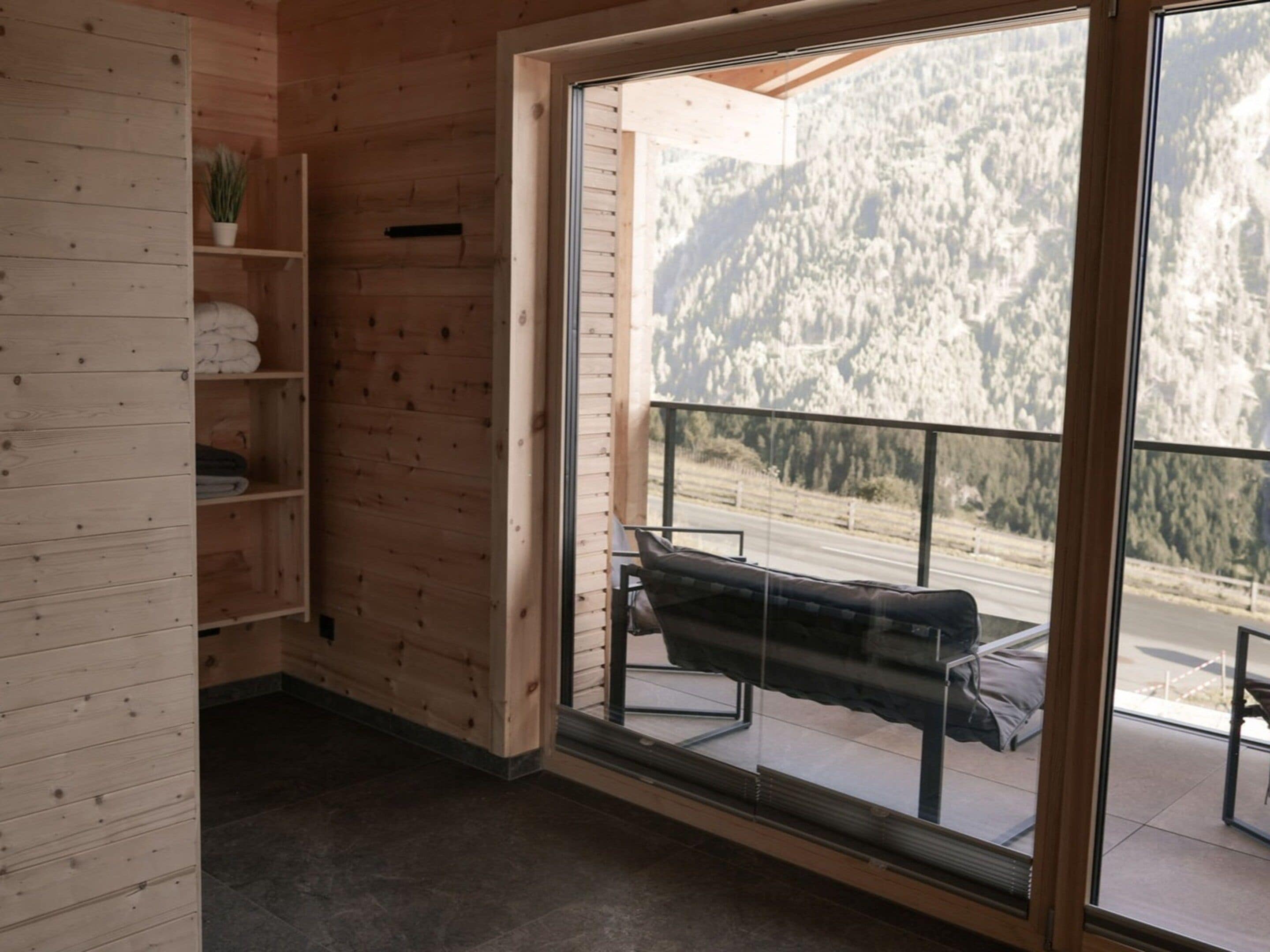 A room with wooden walls, a bench, a shelf with towels, and a large window with a mountain view.