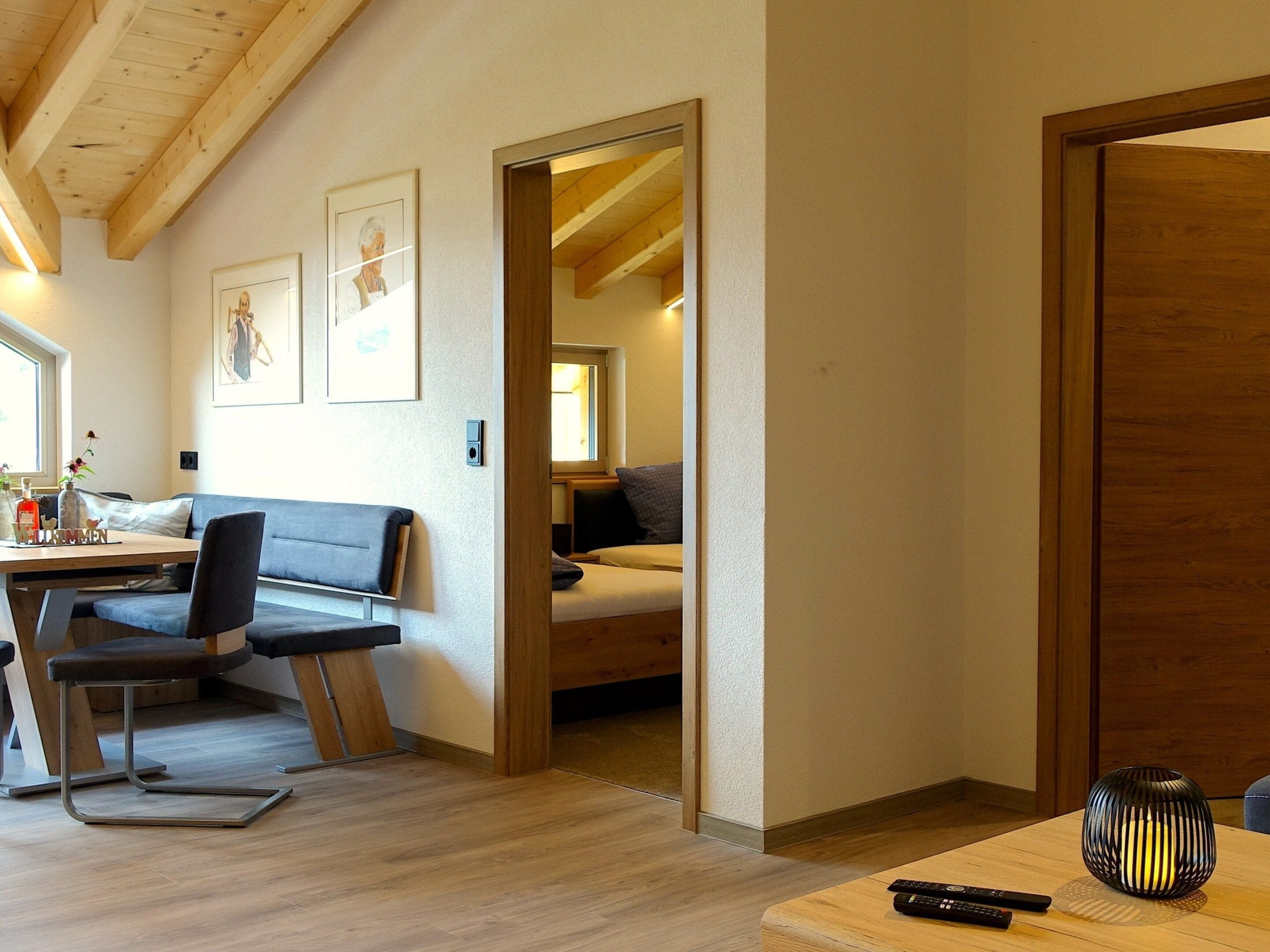 Ein Zimmer mit Holzboden, einer Couch, einem Esstisch mit Stühlen und einem Bett im angrenzenden Raum.