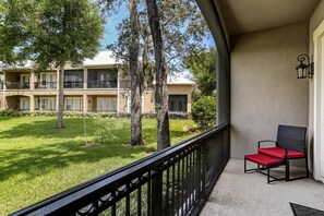 A balcony with a red chair, a view of a building with multiple floors, and a lawn with trees. - Summerwoods 1504 2 Bedroom Condo (Fernandina Beach)