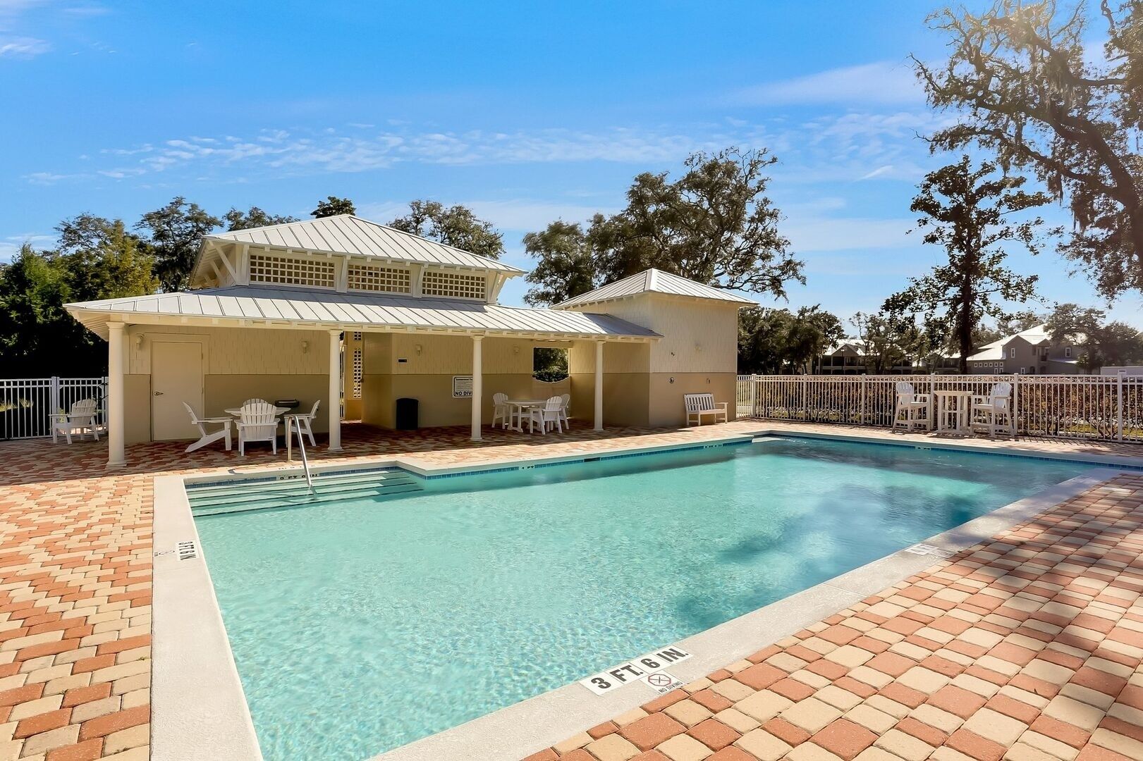 Une piscine rectangulaire dont la profondeur est indiquée par un repère à 3 pieds et 6 pouces, entourée d’une terrasse en briques et de chaises blanches.