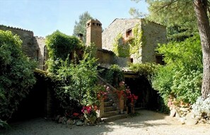 A rustic stone building with a tower, surrounded by lush greenery and flowering plants. - Erbadoro Farmhouse (Umbria)