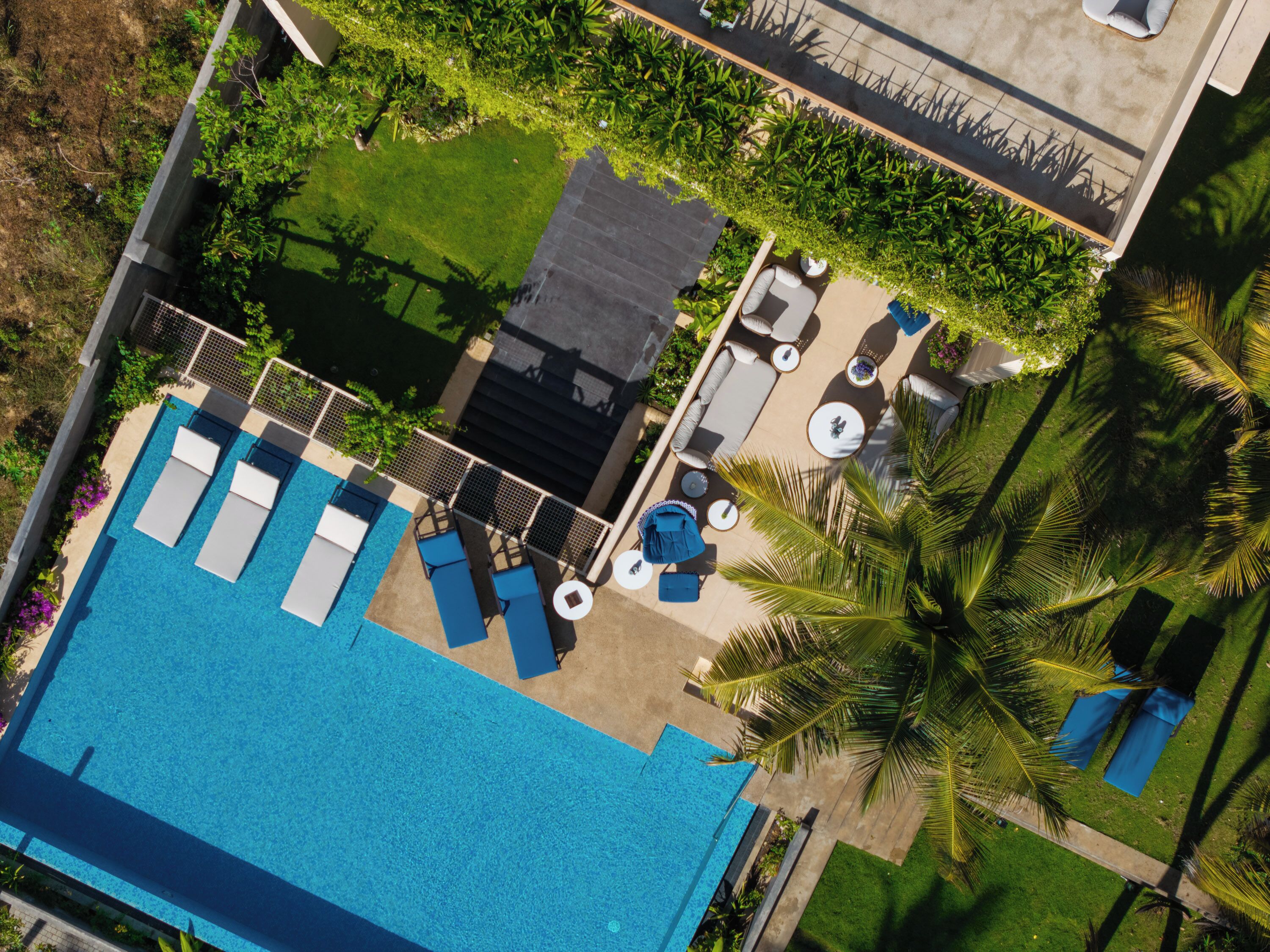 An aerial view of a rooftop pool area with lounge chairs, a small pool, and surrounding greenery.