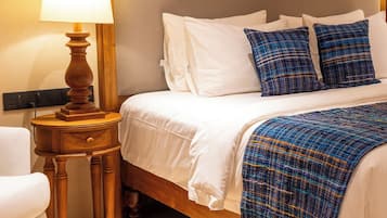 Una cama bien hecha con ropa blanca y almohadas de cuadros azules, una mesita de noche de madera con una lámpara y un cabecero de madera.