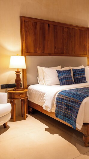 A neatly made bed with white linens and blue plaid pillows, a wooden nightstand with a lamp, and a wooden headboard. - Tombolo Bay (Dikwella)