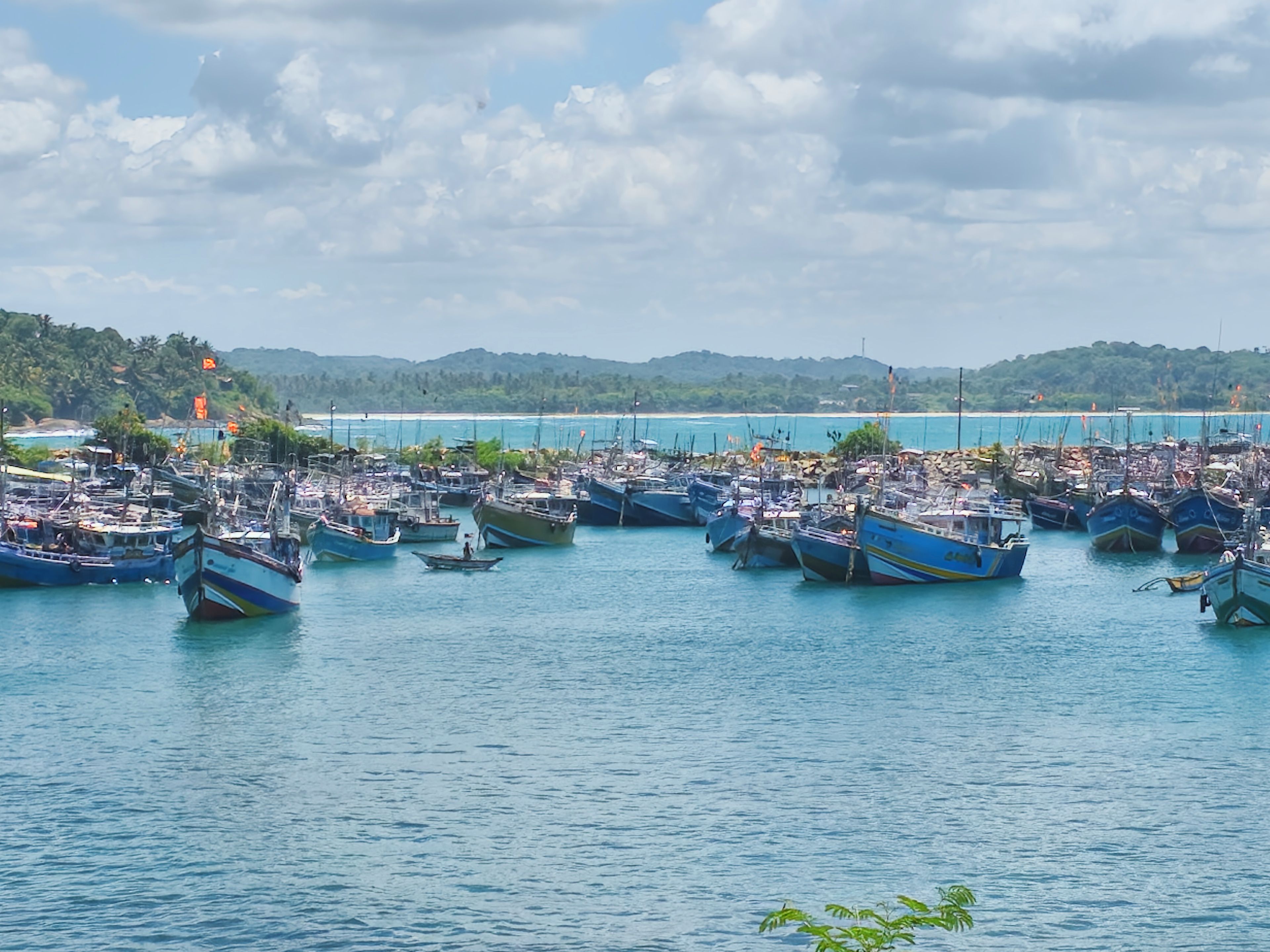 A marina with numerous boats docked, surrounded by water and a hilly landscape in the background.