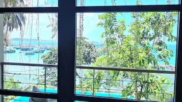 Habitación con vistas a una playa y al océano, que incluye un ventanal grande, dos sillas de mimbre y una mesita.
