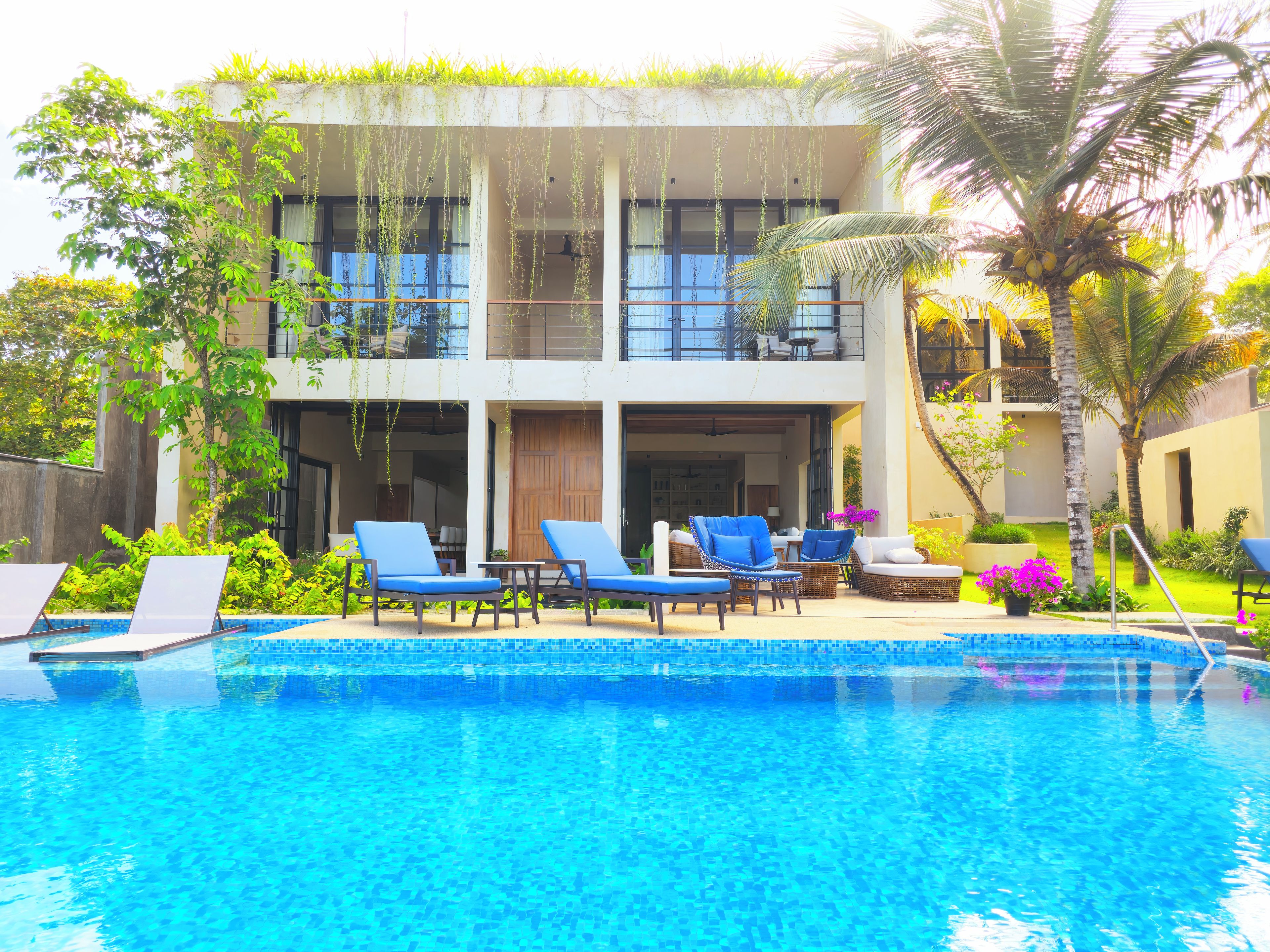Zona de piscina con sillas de descanso, un edificio con balcones y una piscina azul cristalina.