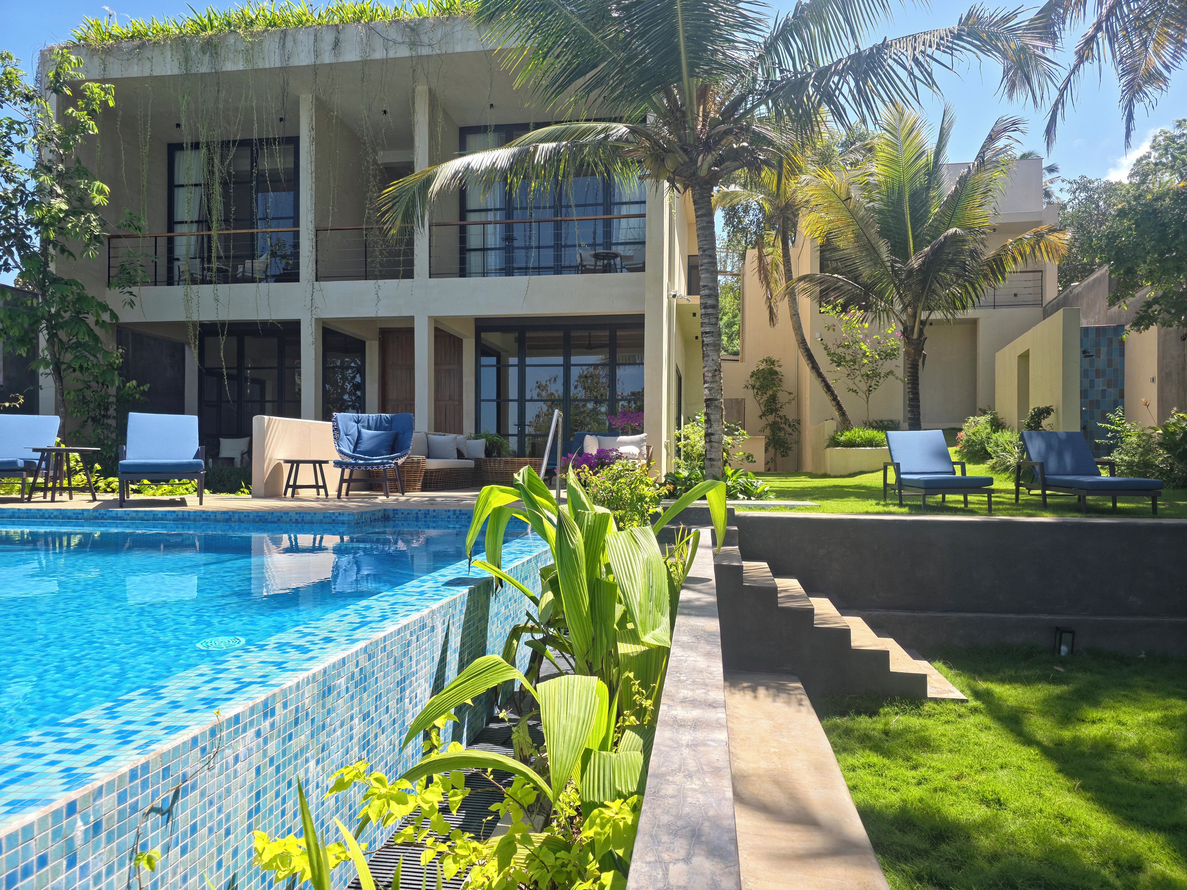 Un espace piscine avec des chaises longues, une piscine carrelée et un bâtiment doté de balcons.
