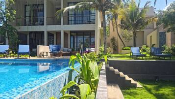 Un espace piscine avec des chaises longues, une piscine carrelée et un bâtiment doté de balcons.
