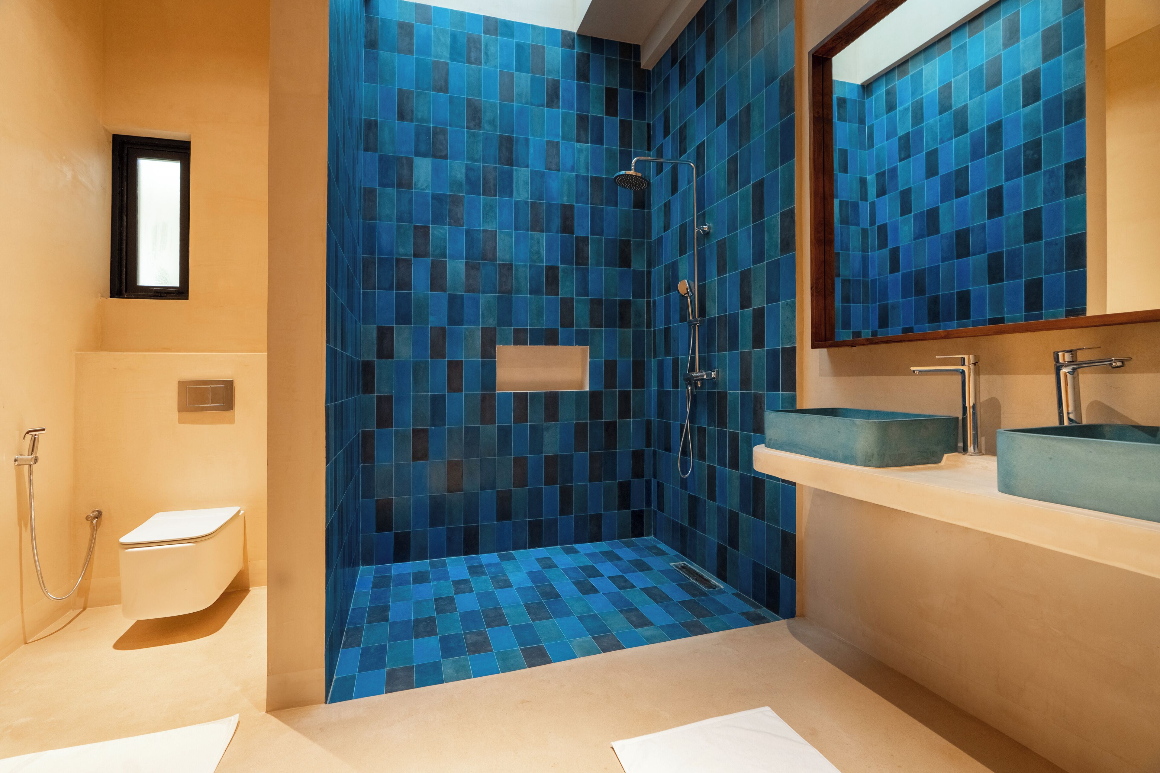 Un baño con ducha de azulejos azules, inodoro blanco y lavabo con recipiente azul.