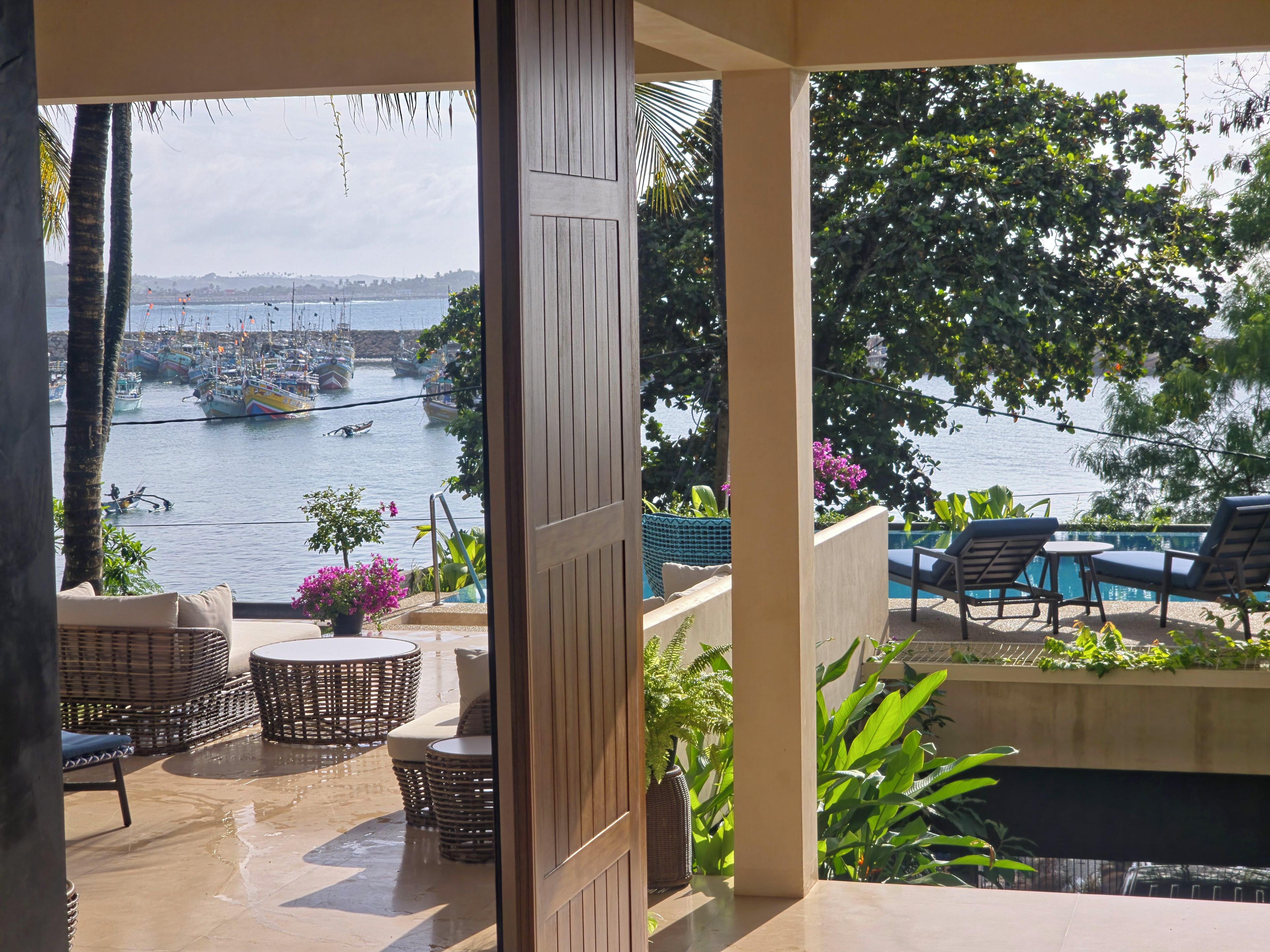 A terrace with wicker furniture, a pool, and a view of boats on the water.