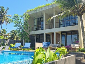 A two-story building with a swimming pool, lounge chairs, and tropical plants. - Tombolo Bay (Dikwella)