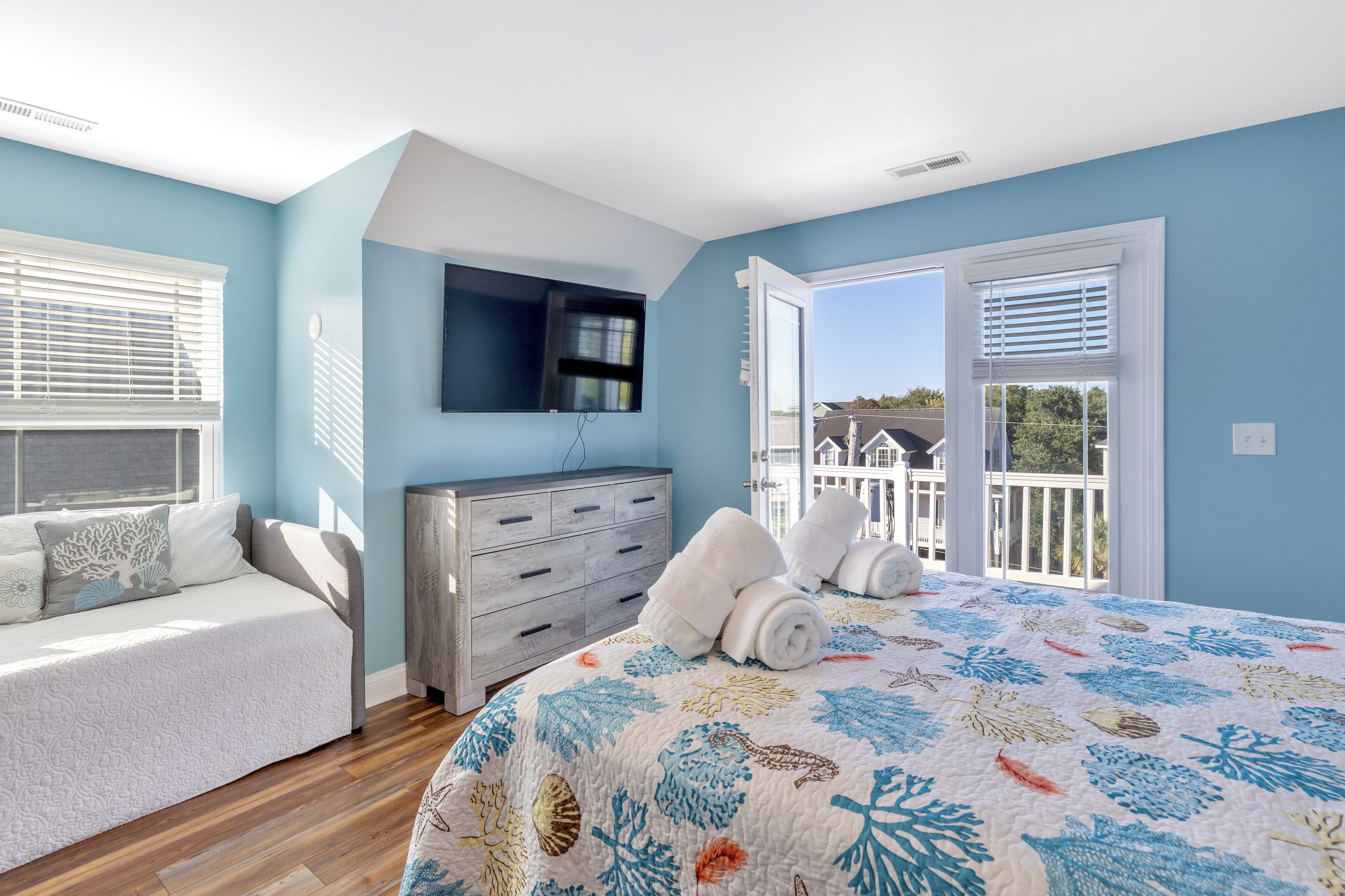 Un dormitorio con cama, cómoda, televisor y balcón.