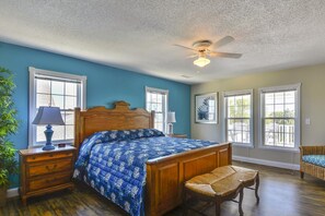 Ein Schlafzimmer mit einem hölzernen Bett, einem Deckenventilator und Blick durch große Fenster.