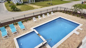 A swimming pool with two separate sections, surrounded by a black metal fence. There are lounge chairs and a stop sign visible in the background. - Coastal Treasure: Steps to Beach & Pool (Murrells Inlet)