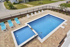 Piscina com duas áreas distintas, rodeada por uma cerca de metal preto. Há espreguiçadeiras e uma placa de pare visíveis ao fundo.